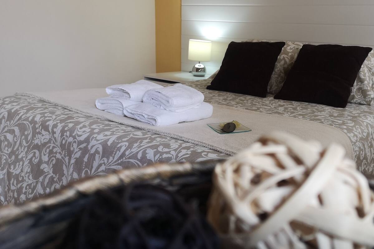 A neatly made bed with folded towels, a bedside lamp, and patterned bedding.