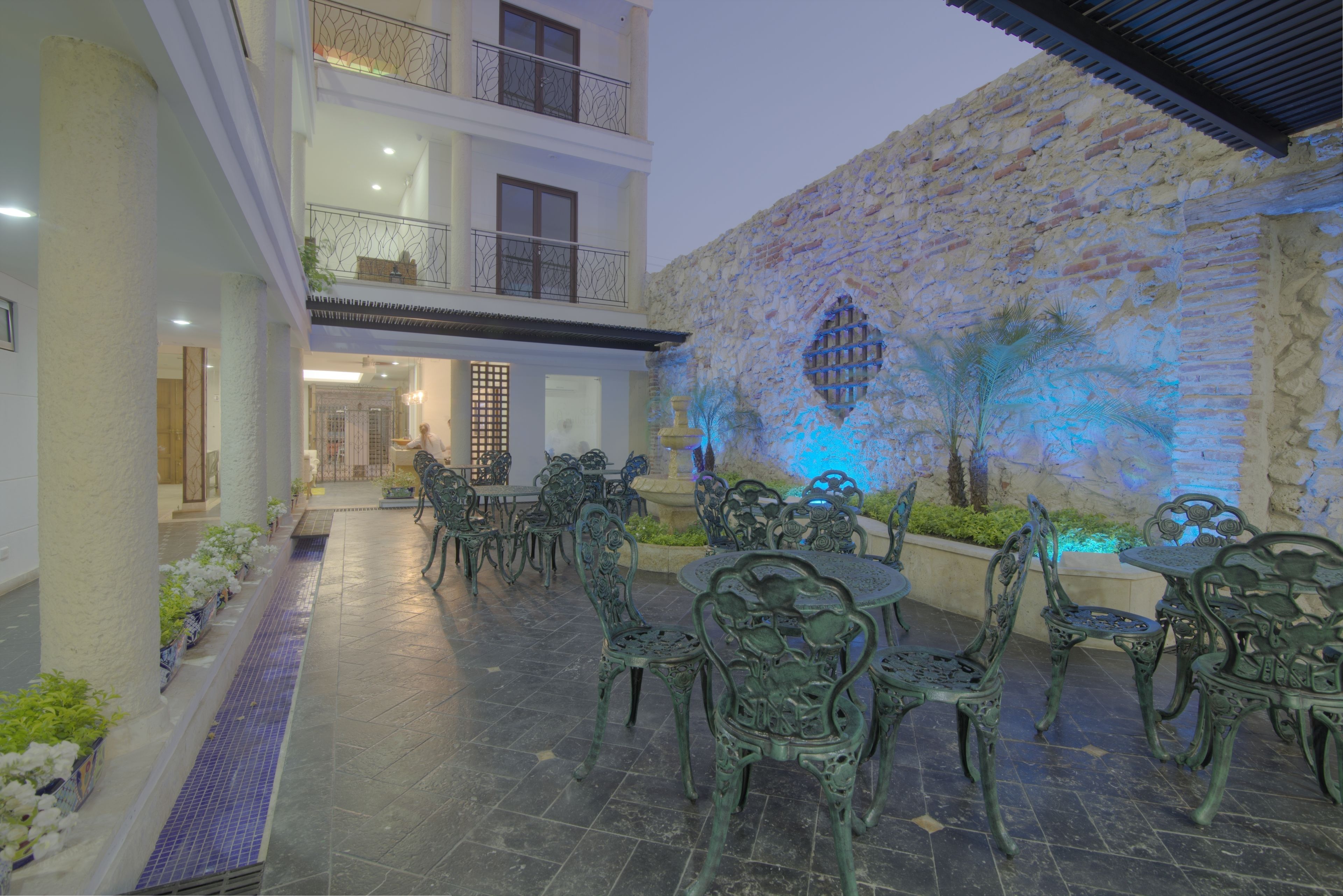 Une terrasse extérieure agrémentée de chaises et de tables en métal ouvragé, d’un mur en pierre et d’un balcon doté de balustrades.