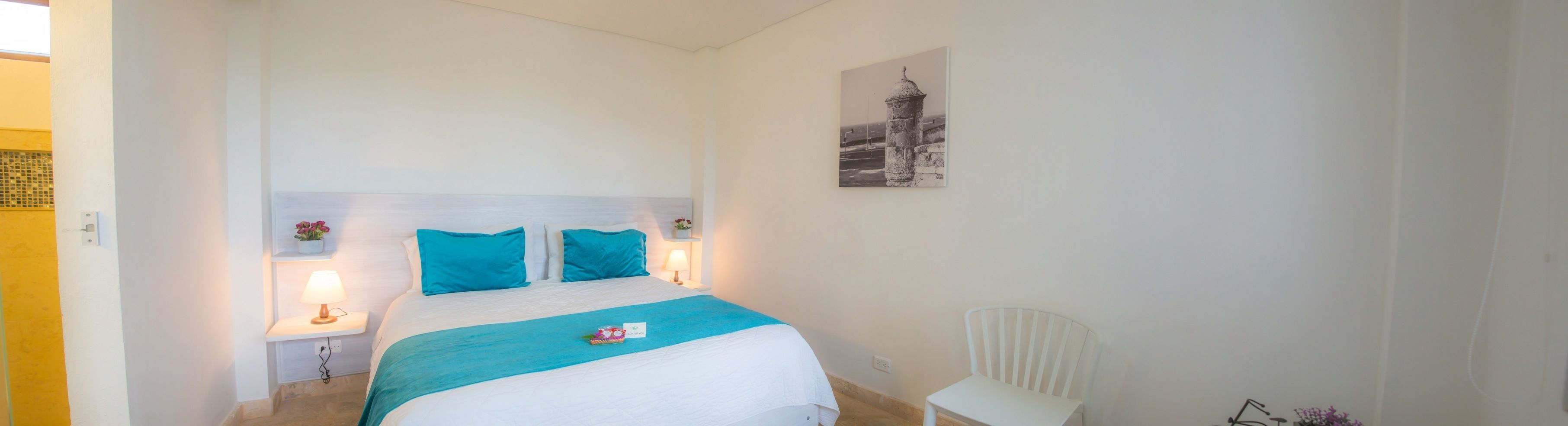 Una camera da letto con un letto, un comodino, una sedia e un quadro appeso al muro.