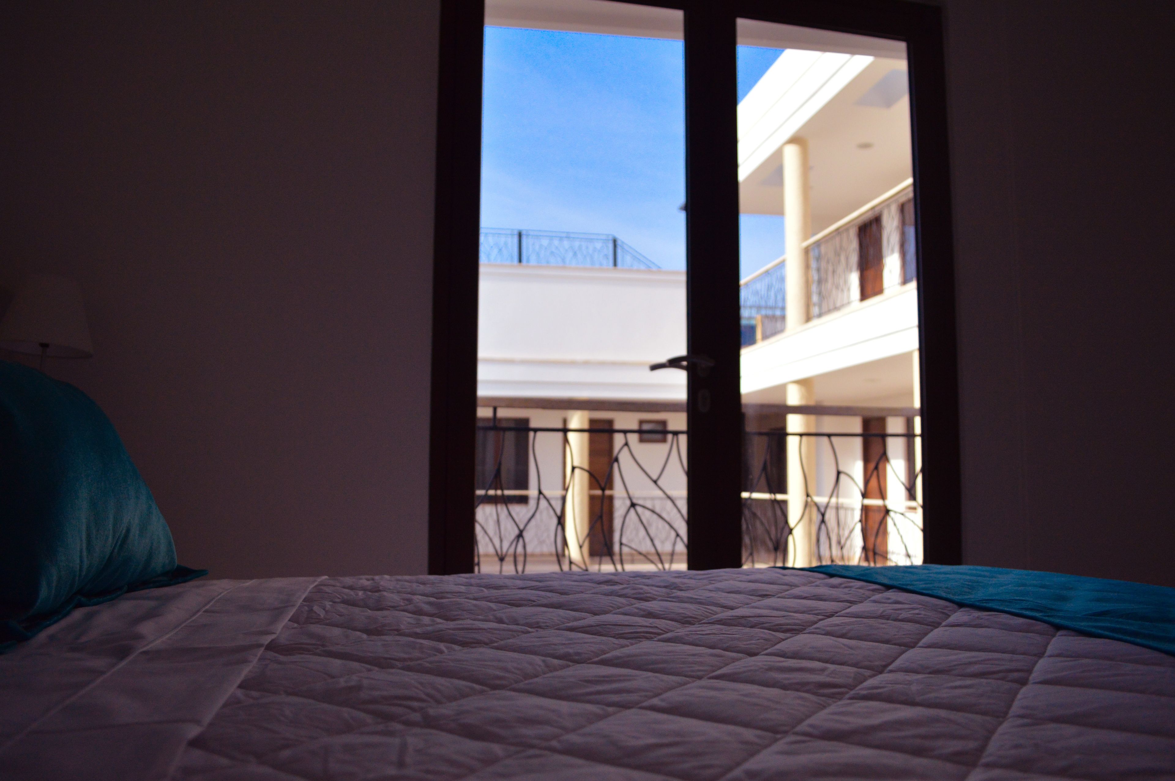 Une chambre avec un lit, donnant sur un balcon extérieur, et une porte menant à une autre pièce.