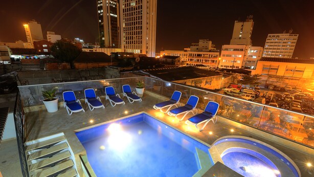 A rooftop pool with blue lounge chairs and a hot tub, surrounded by city buildings at night. - Hotel Boutique La Artillería (Cartagena)