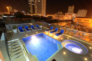 A rooftop pool with blue lounge chairs and a hot tub, surrounded by city buildings at night. - Hotel Boutique La Artillería (Cartagena)
