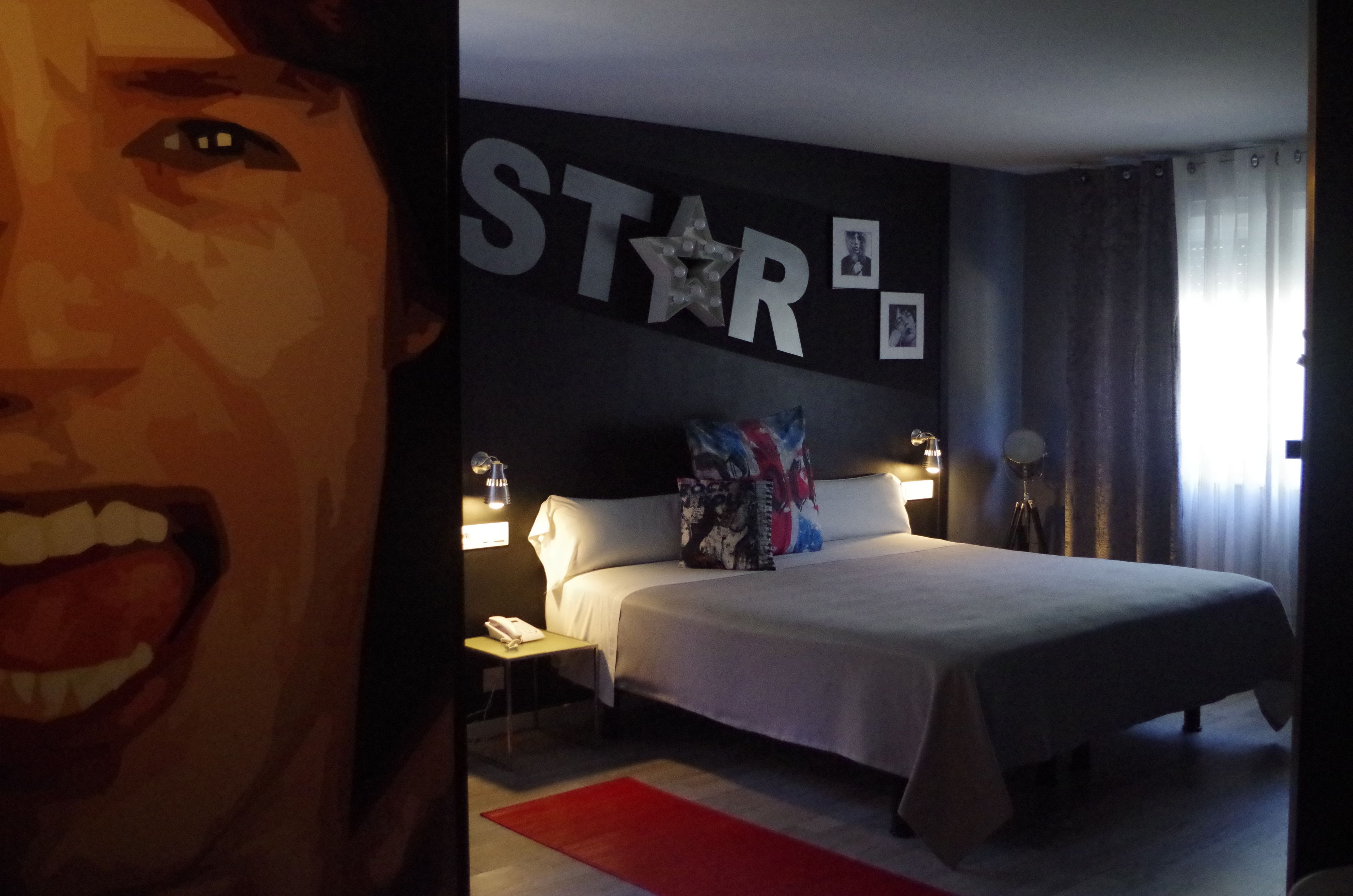 A hotel room with a bed, bedside tables, a wall with a 'STAR' sign, and a window with curtains.