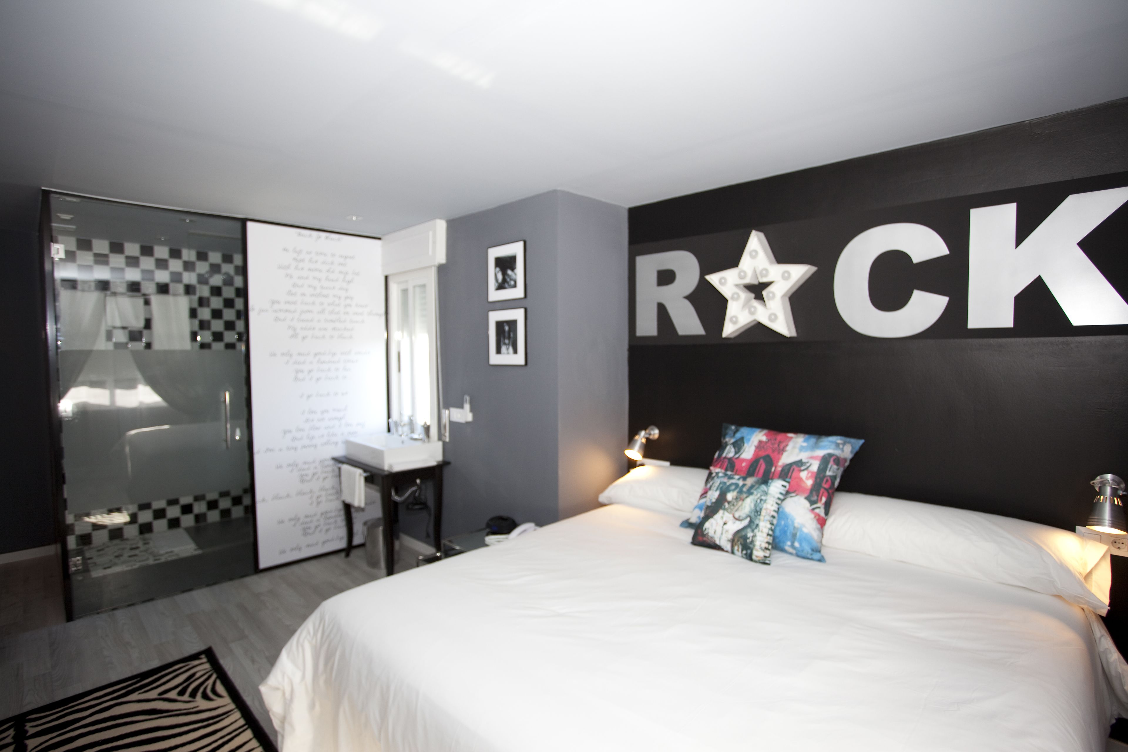 A bedroom with a bed, a desk, a mirror, and a wall with the word "ROCK" and a star decoration.