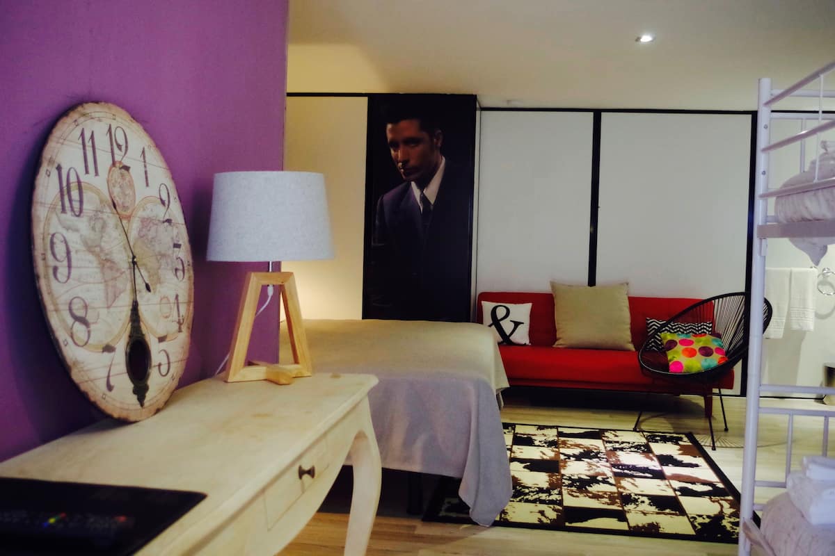 Una habitación con un reloj grande, una cama, un sofá rojo, una silla y un cuadro en la pared.