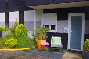 A small outdoor seating area with a chair and a table, a potted plant, and a door with a window above it. - HOTEL Rock Star (Taboadela)