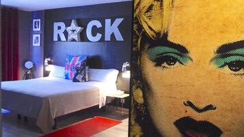 A hotel room with a bed, a nightstand, a lamp, and a wall with the word "ROCK" and a star.