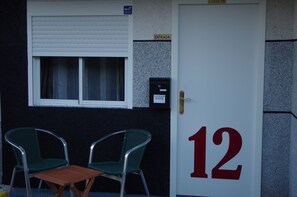 A door with the number 12, a window with blinds, two green chairs, and a small table. - HOTEL Rock Star (Taboadela)