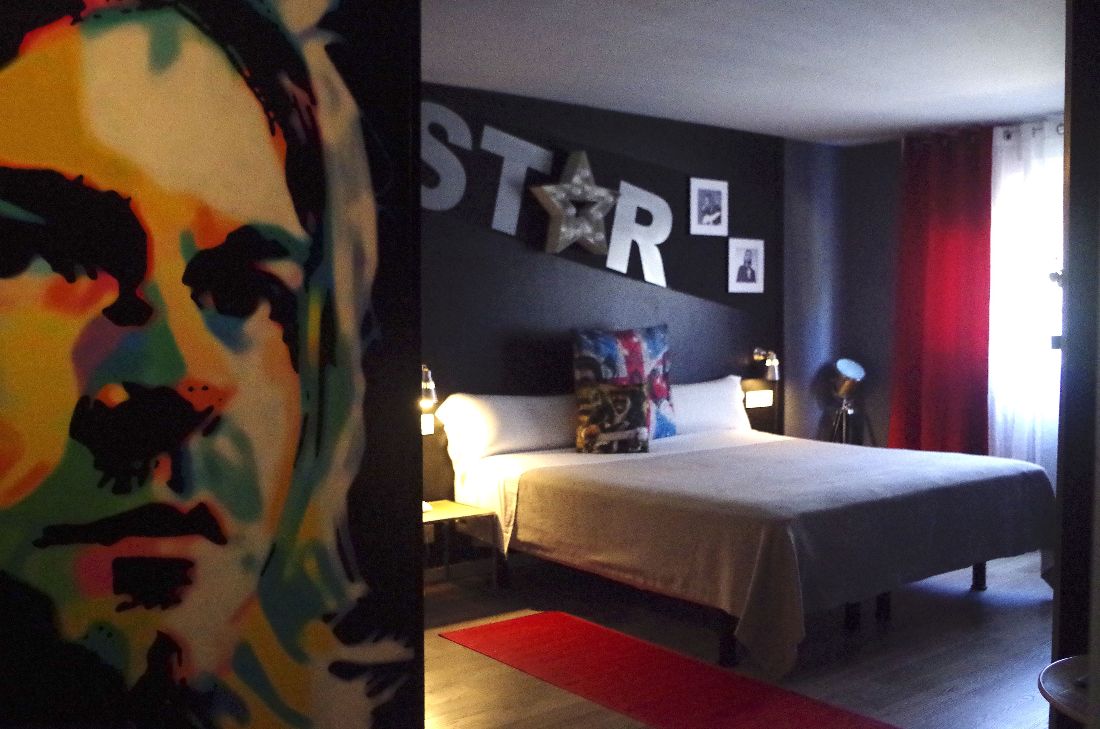 Une chambre à coucher avec un lit, une table de chevet, une lampe et un mur décoré d’étoiles.