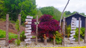 Un jardín con señalización, una estructura de madera y un árbol de hojas rojas.