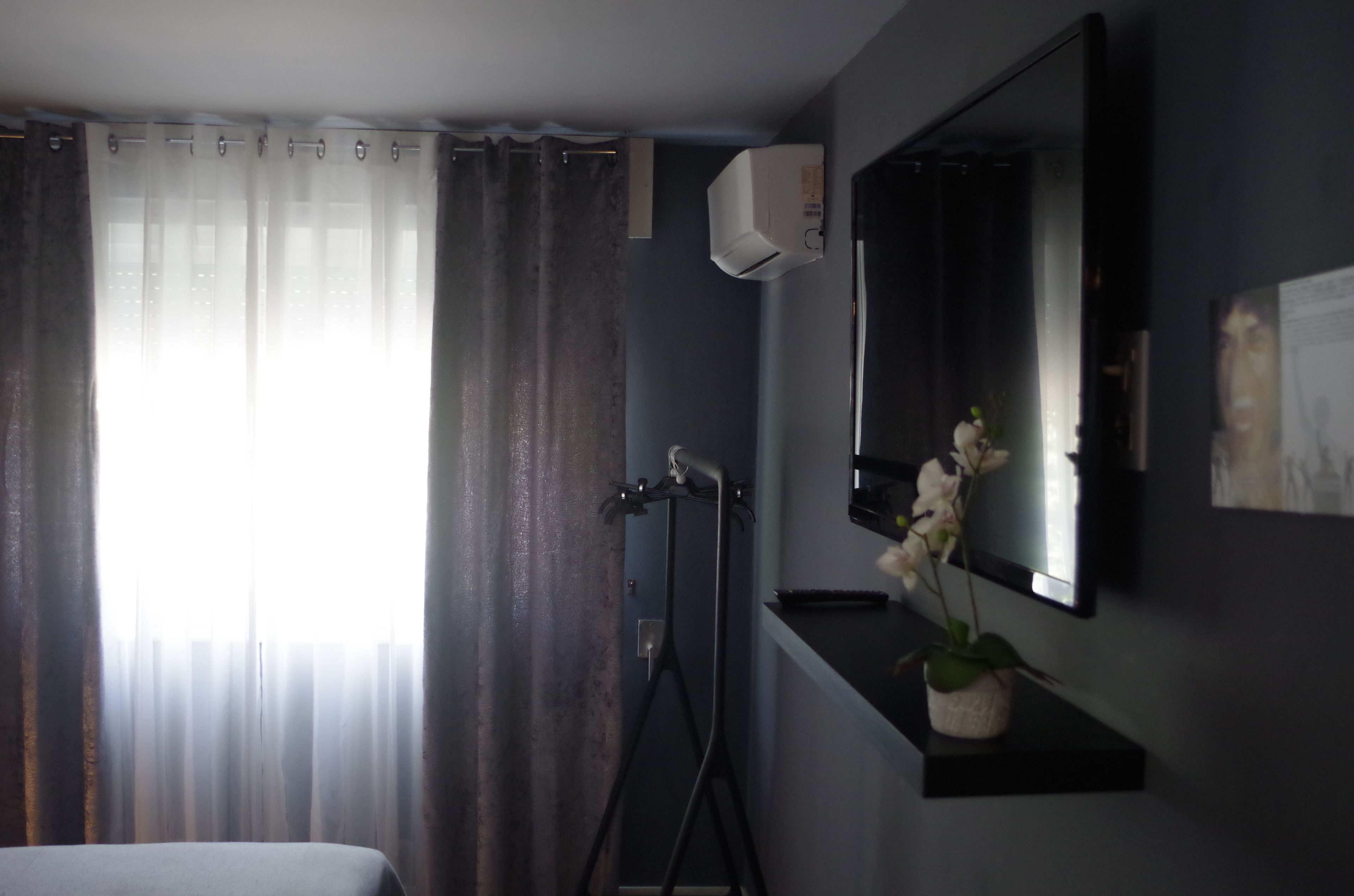 A room with a bed, a mounted air conditioner, a mirror, and a potted orchid.
