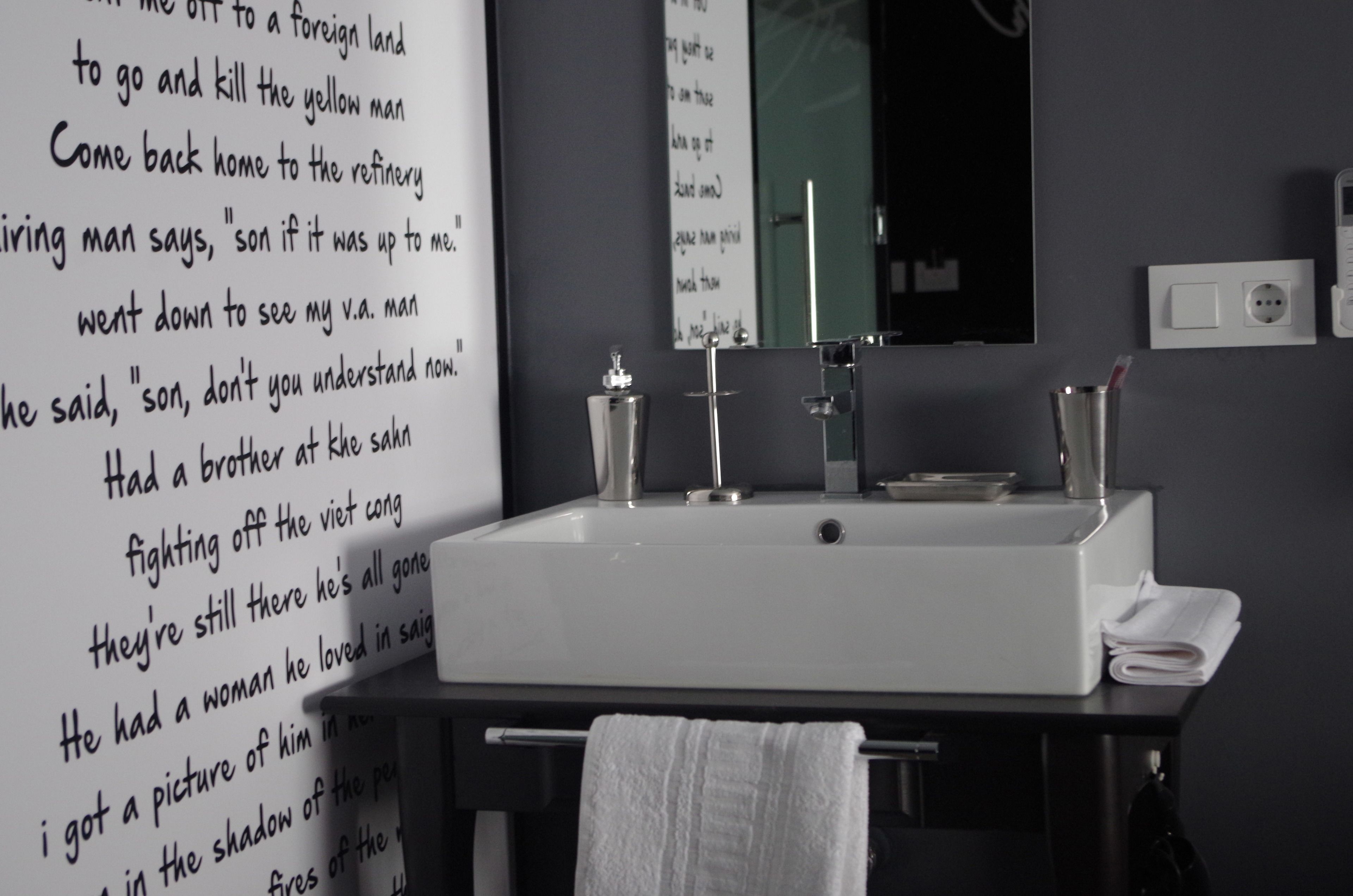 Une salle de bain avec un lavabo blanc, un miroir et un robinet fixé au mur. Une serviette est suspendue à un porte-serviettes et une autre serviette blanche est posée sur le lavabo.