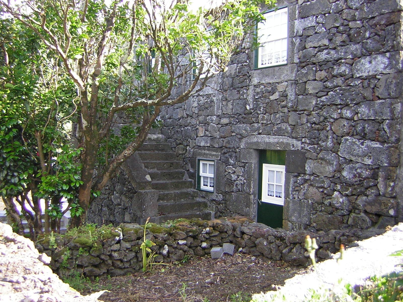 Un bâtiment en pierre avec une petite fenêtre et une porte, entouré de verdure.