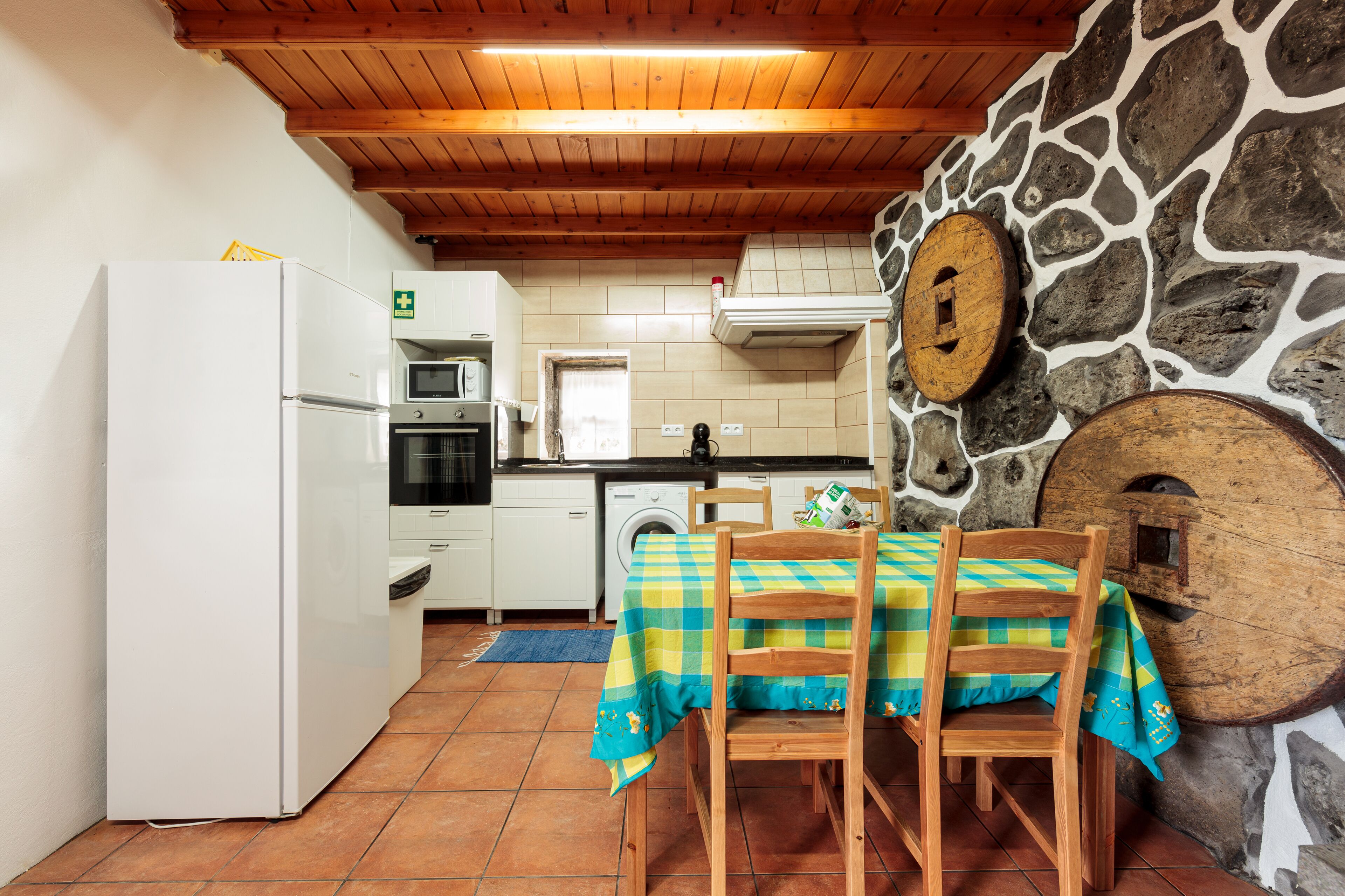Una cocina con pared de piedra, techo de madera y una mesa con mantel a cuadros.