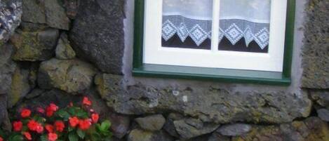 Mur de pedra amb una finestra que té un marc blanc i un cortinet de punt de festa.