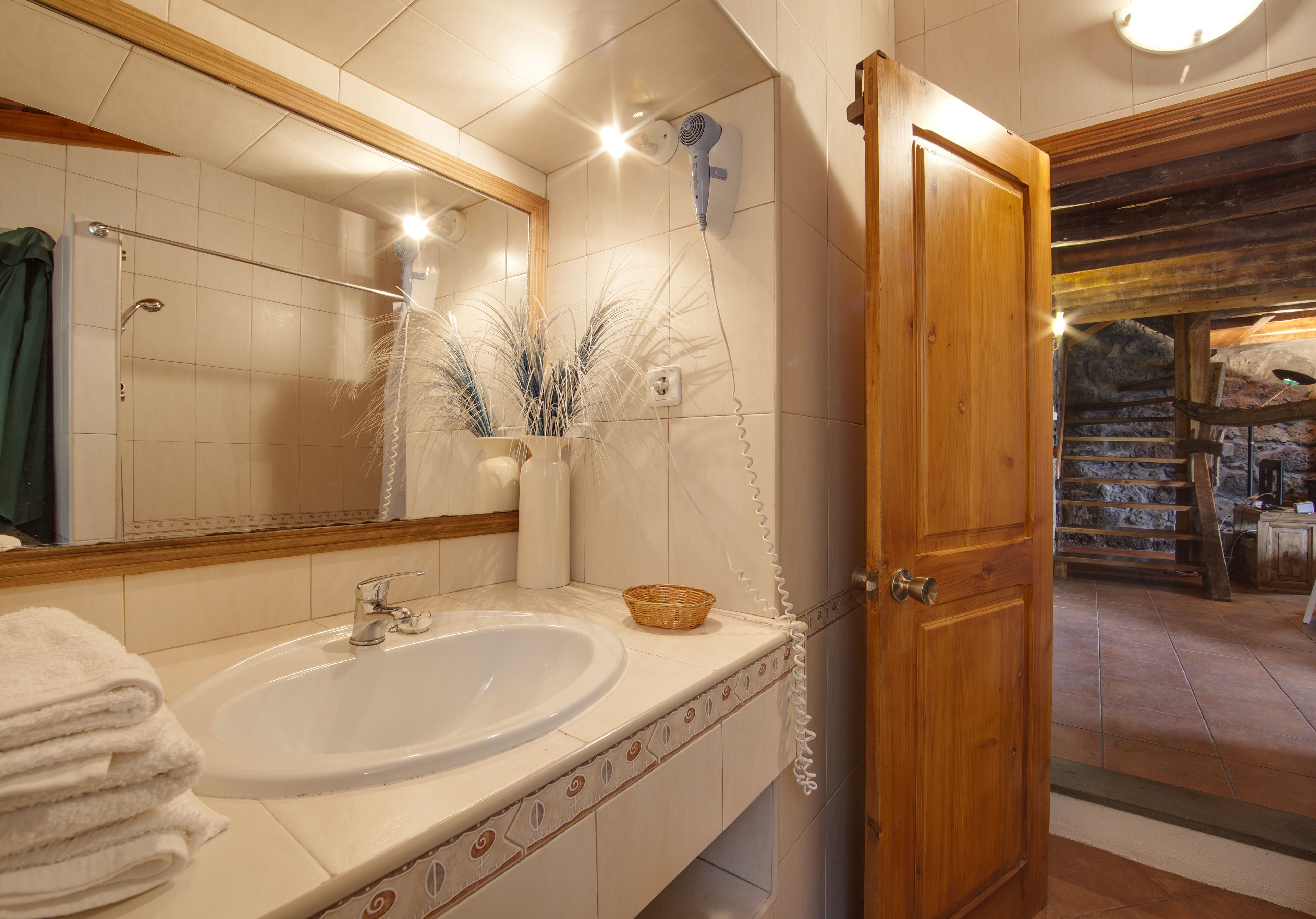 Een badkamer met een wastafel, spiegel en een houten deur die leidt naar een stenen trap.