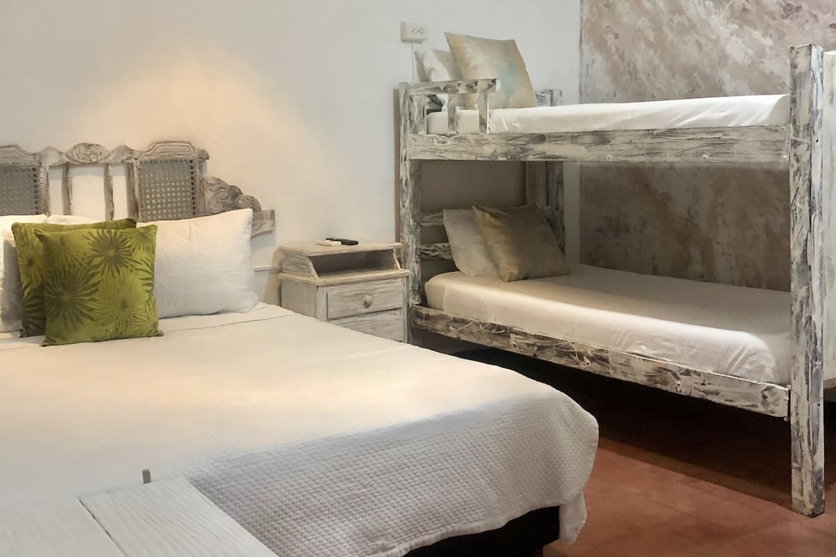 Une chambre avec un lit superposé, un lit simple, une table de chevet et une lampe.