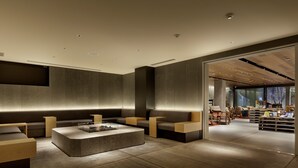 A modern interior with a seating area, a coffee table, and a view into another room with a desk and chairs. - Piece Hostel Sanjo (Kyoto)