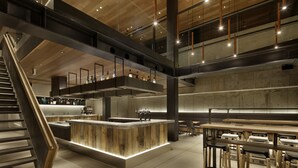 A modern interior with a central island bar, high ceilings, and exposed structural elements. - Piece Hostel Sanjo (Kyoto)