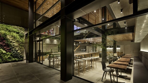 An indoor dining area with modern furniture and a glass wall overlooking a green space. - Piece Hostel Sanjo (Kyoto)