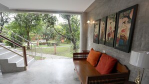 A spacious room with a wooden sofa, a staircase leading to an outdoor area, and a wall adorned with framed artwork. - GongKaew HuenKum Hotel (Chiang Mai)