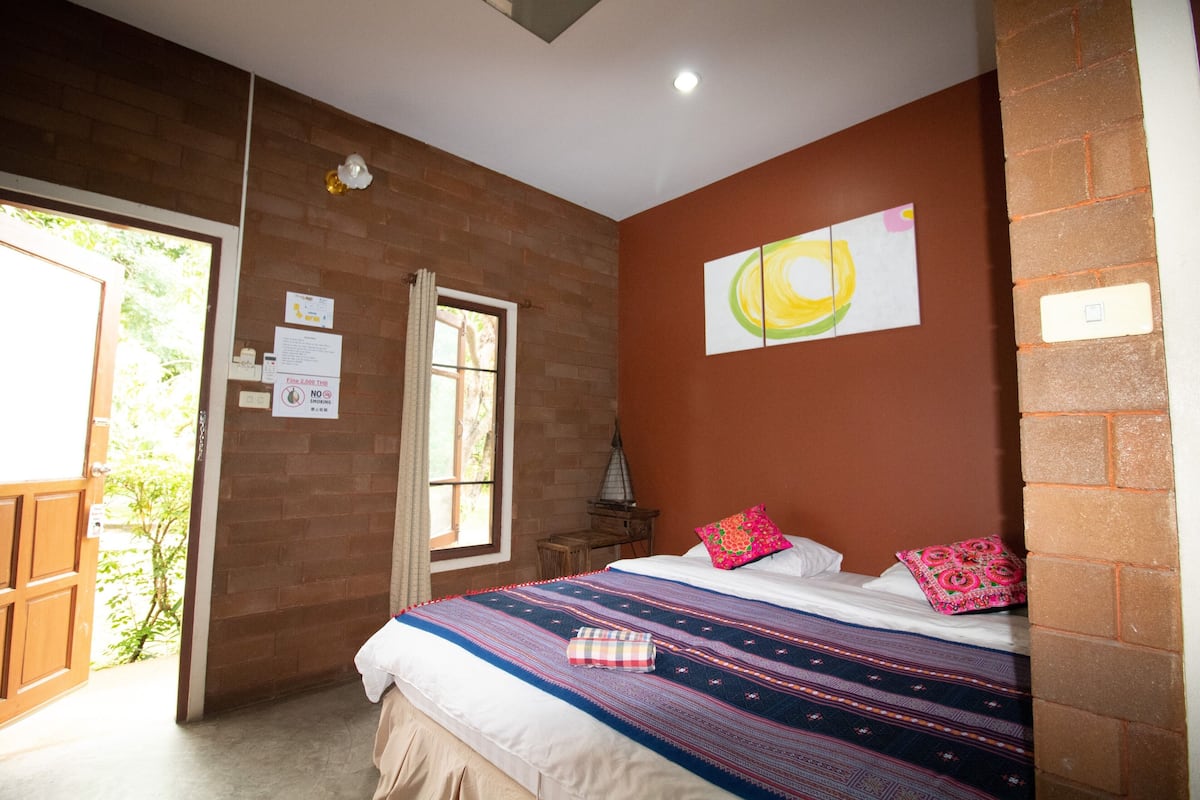 A bedroom with a large bed, a window, a brick wall, and a painting.