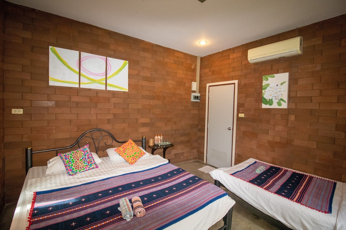 A room with two beds, a brick wall, a door, and a wall-mounted air conditioner.