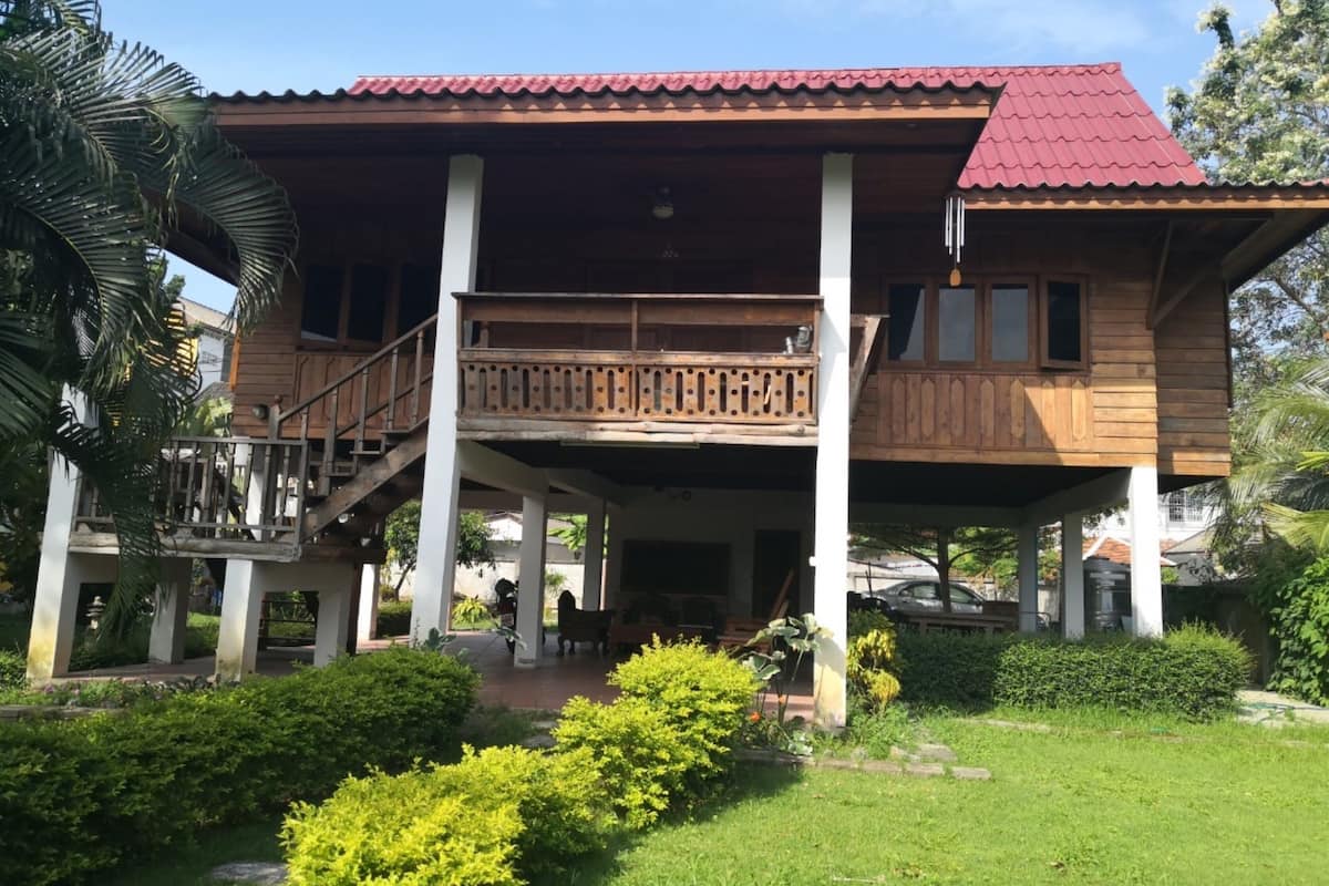 A wooden house with a red roof, a balcony, and a covered porch area.