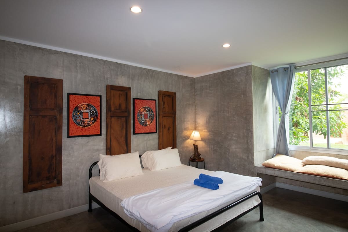 A bedroom with a bed, a window with a view, and artwork on the wall.