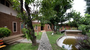 A courtyard with a brick building, a hexagonal paved walkway, a small pond, and a bench. - GongKaew HuenKum Hotel (Chiang Mai)