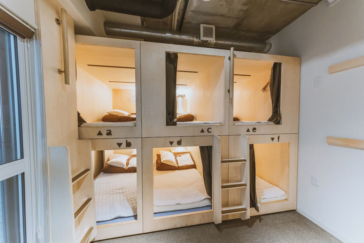A room with four wooden bunk beds, each with a small window and labeled with letters.