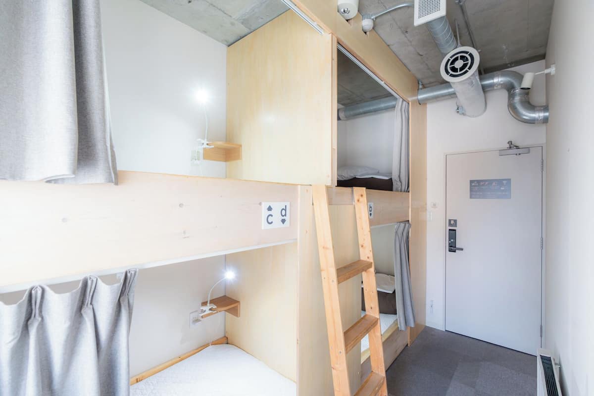 A bunk bed room with a wooden ladder, a door with a sign, and a ventilation system.