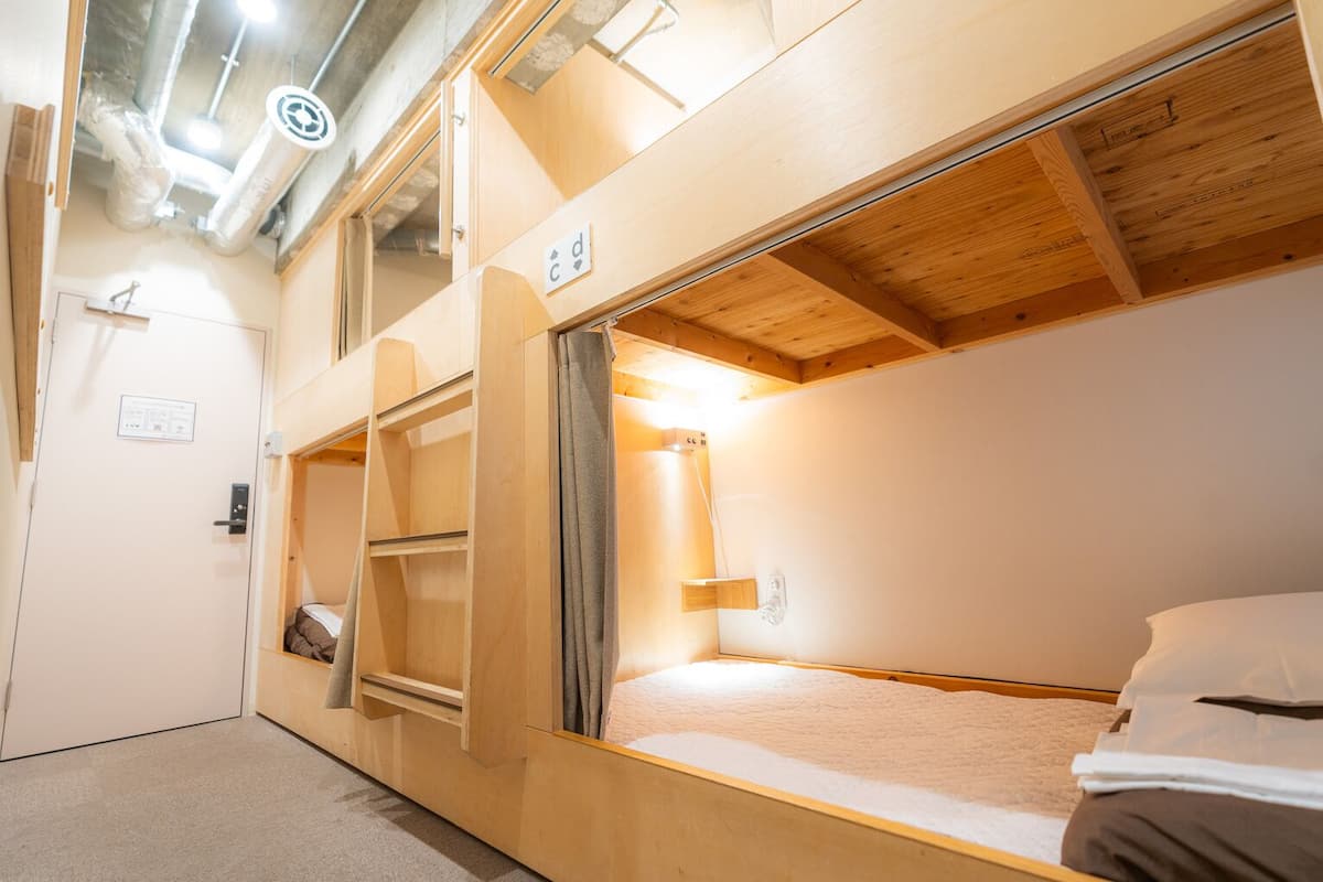 A bunk bed room with a wooden ceiling, a small shelf, a wall-mounted light, and a door with a sign.