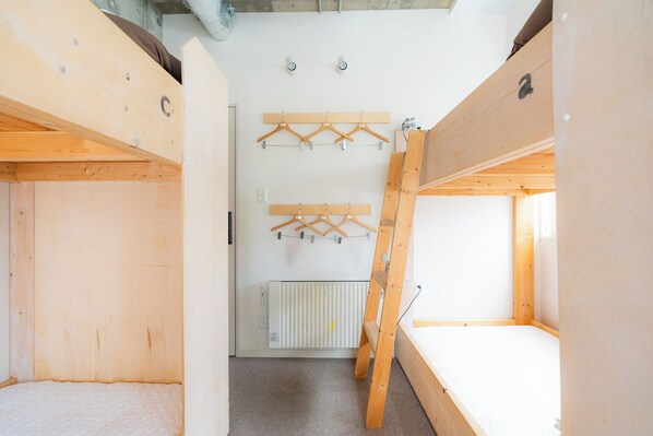 A room with a bunk bed, wooden walls, a radiator, and wooden hangers on a rack. - Grand Hostel LDK Sapporo (Sapporo)