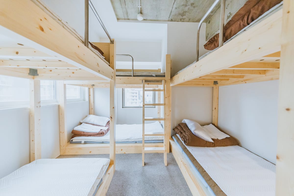 A bunk bed room with a ladder, a window, and a view of the city.