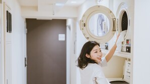 Una persona utilizando una lavadora de carga frontal en un cuarto de lavado bien iluminado, con una puerta al fondo.