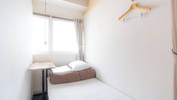 A small, neatly arranged bedroom with a single bed, a bedside table, a hanging light, and a wooden hanger on the wall.