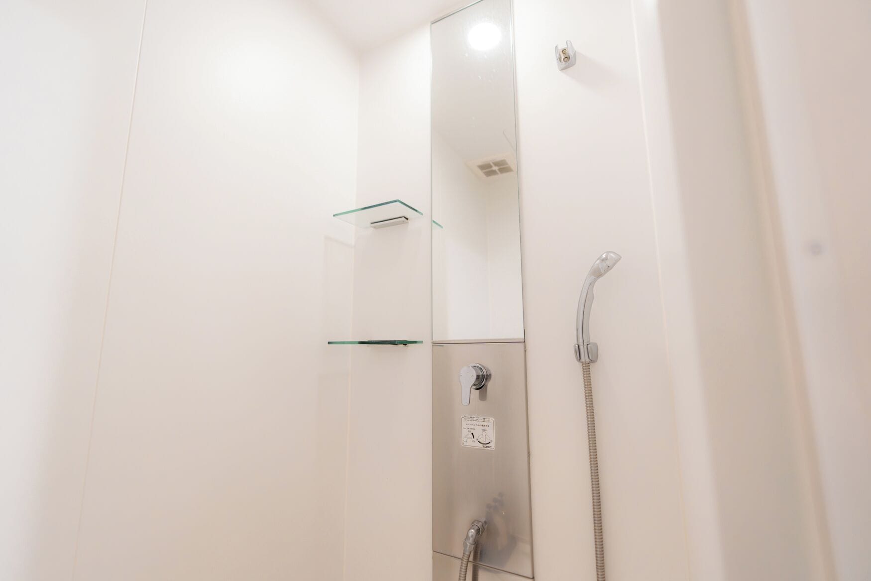 A modern bathroom with a glass shower enclosure, a handheld showerhead, and a wall-mounted faucet.