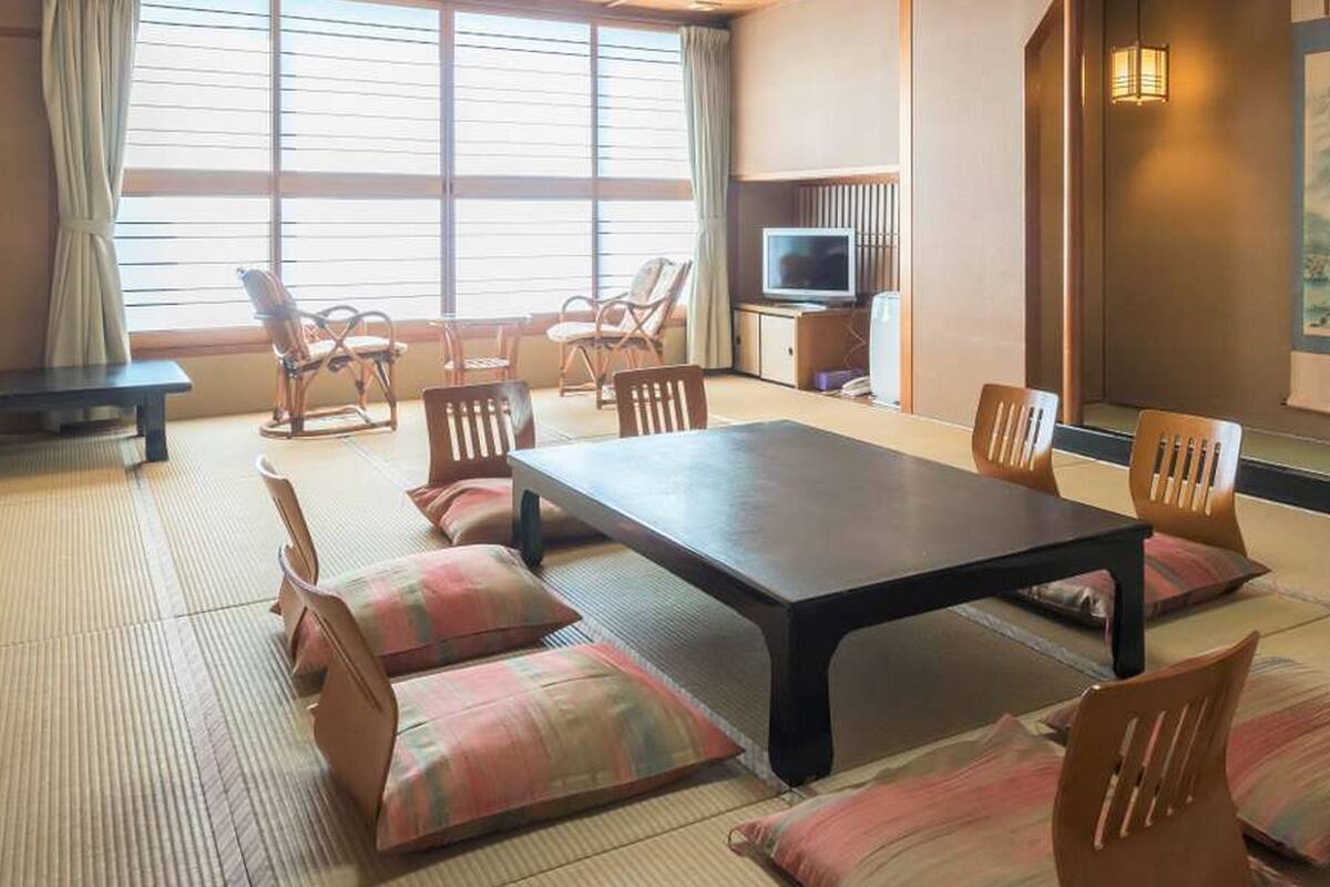 A traditional Japanese-style room with tatami flooring, a low table, and wooden chairs.