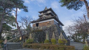 A traditional Japanese building with a stone base and wooden upper structure, surrounded by trees and a clear sky. - Awara Grand Hotel (Awara)