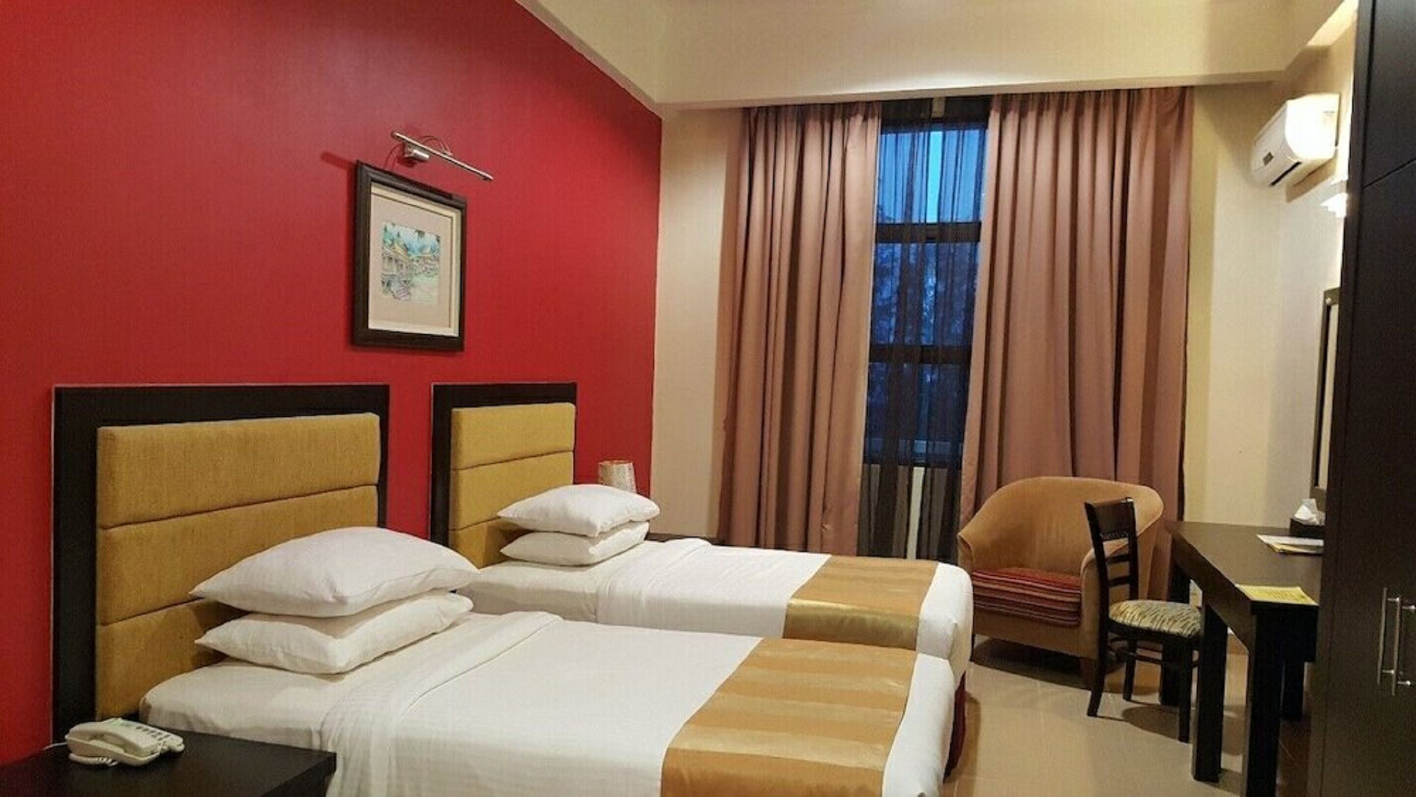 A hotel room with two beds, a desk, a chair, a telephone, and a window with curtains.