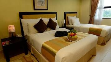 A hotel room with two beds, a nightstand with a lamp, a framed picture on the wall, and a fruit bowl on the bed.