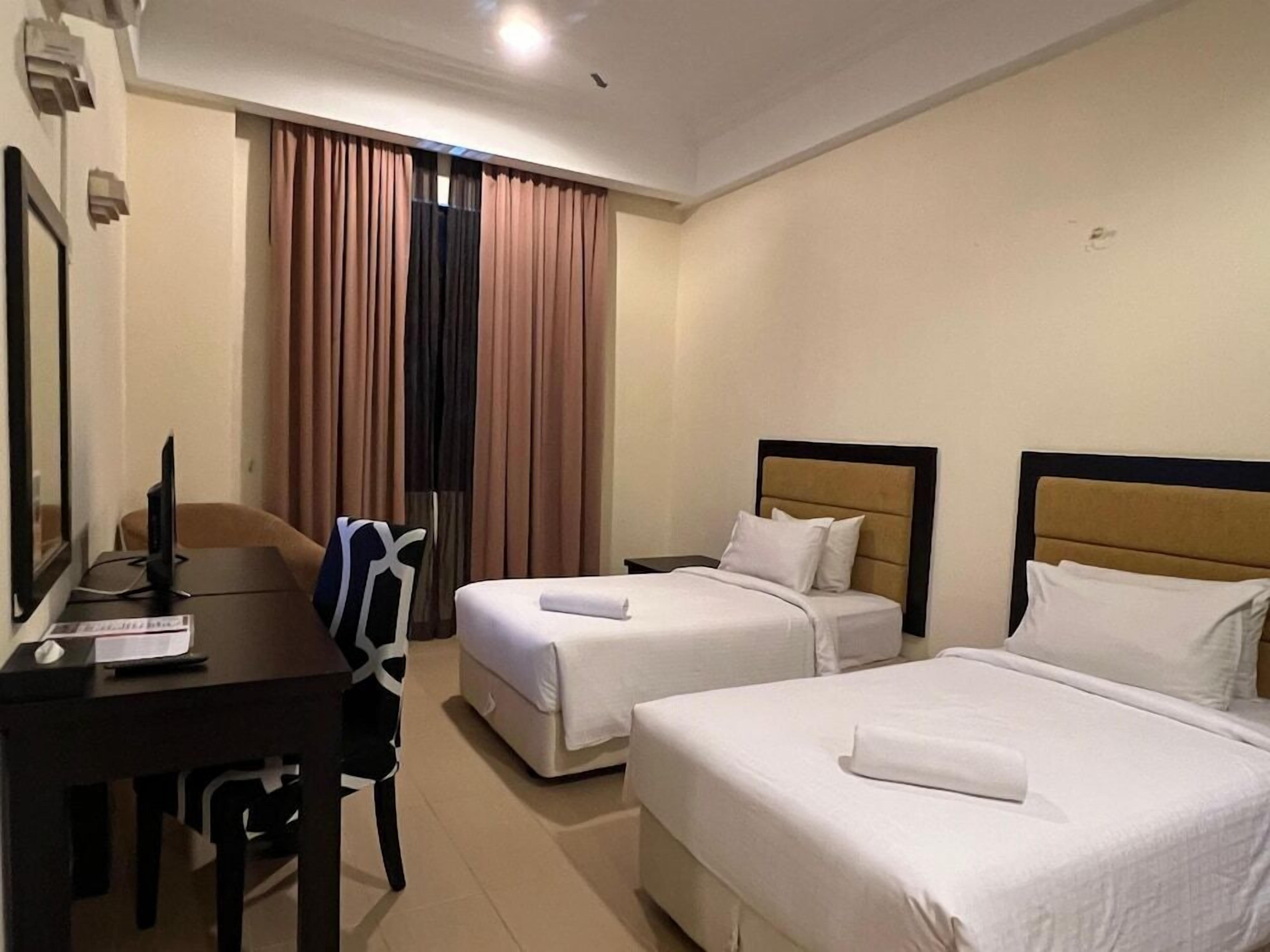 A hotel room with two beds, a desk with a computer, and a chair.