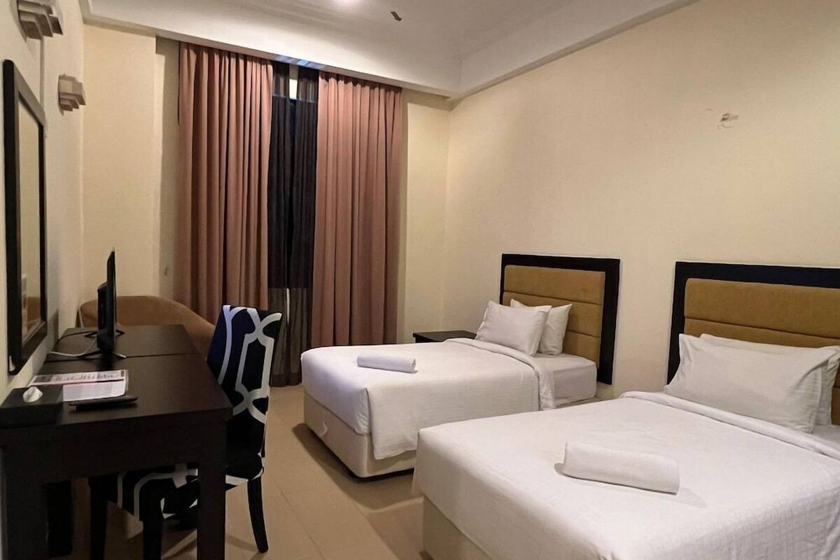 Ein Hotelzimmer mit zwei Betten, einem Schreibtisch mit einem Computer und einem Stuhl.