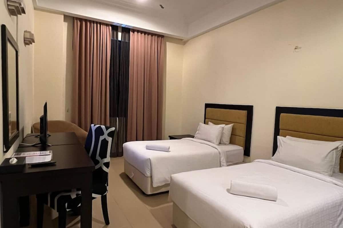A hotel room with two beds, a desk with a computer, and a chair.