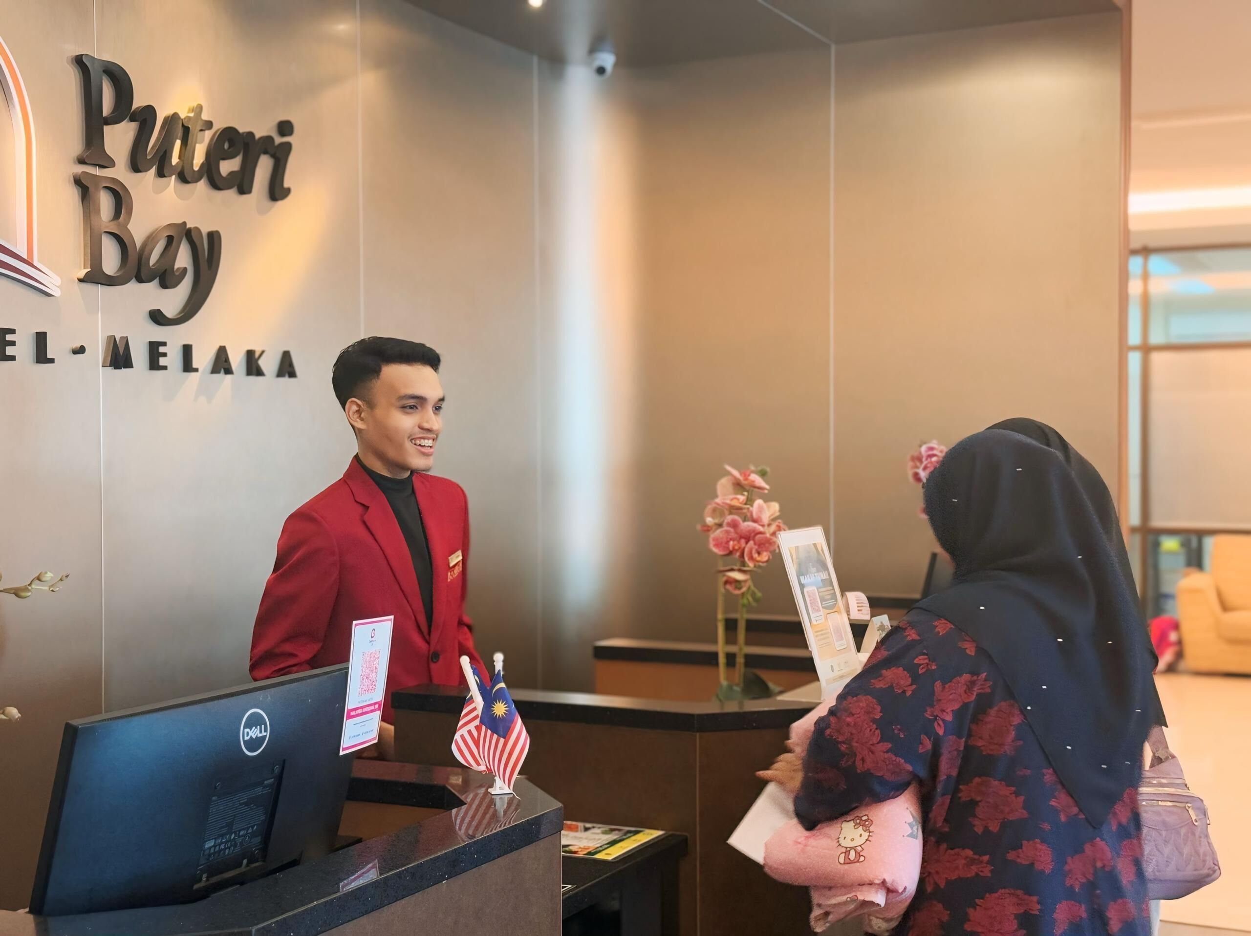 A hotel reception desk with a sign reading "Puteri Bay" and "EL-MELAKA".