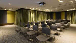 A conference room with rows of chairs, a projector on the ceiling, and curtains on the walls. - The Lime Boutique Suites (Hyderabad)