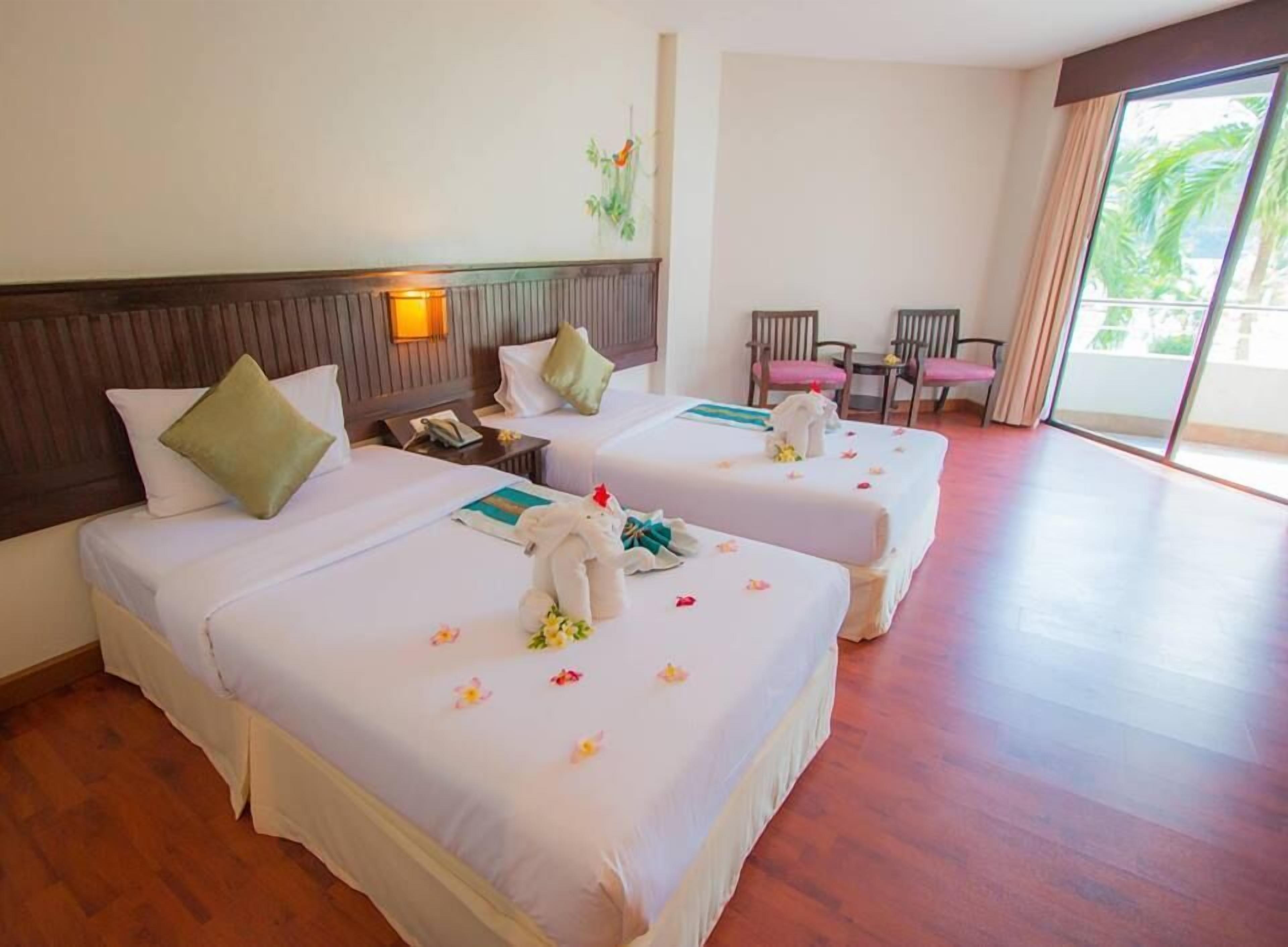 Une chambre d’hôtel avec deux lits, une petite table, des chaises et une grande fenêtre.
