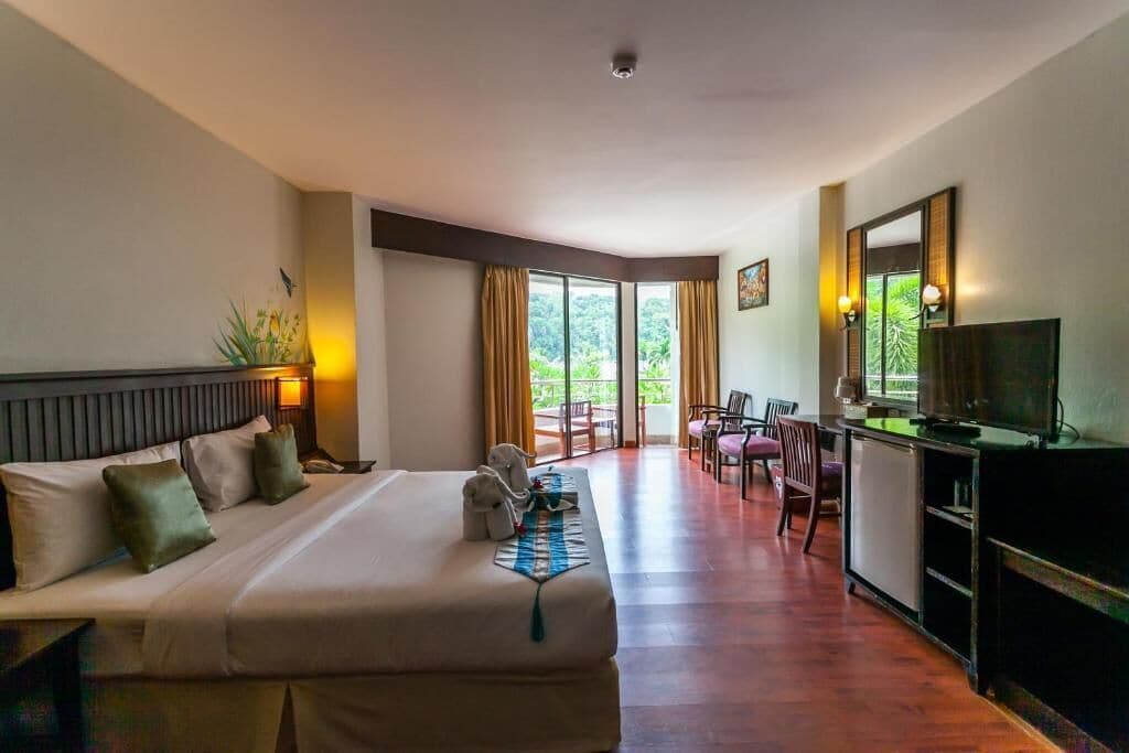 Een hotelkamer met een groot bed, een bureau met een televisie, en uitzicht op het omliggende landschap door de ramen.