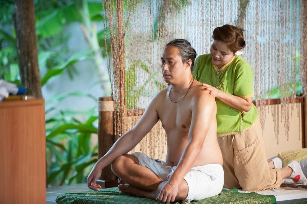A person receiving a massage in a room with a wooden cabinet and a curtain with hanging elements.